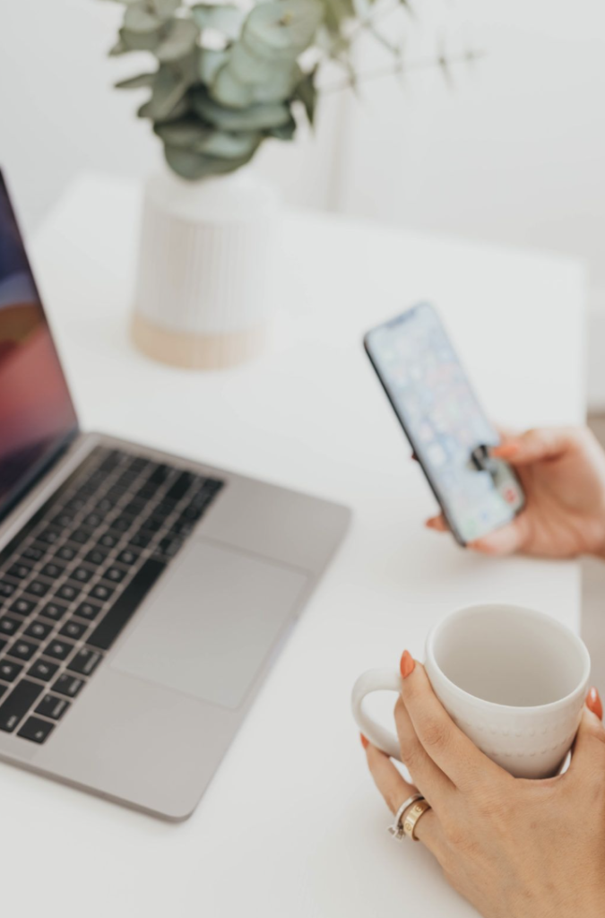 Femeie cu telefonul lângă laptop și cafea